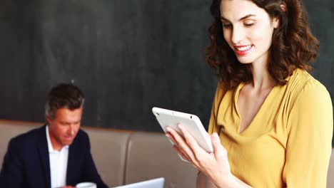 Businesswoman-using-digital-tablet-while-colleague-working-in-background