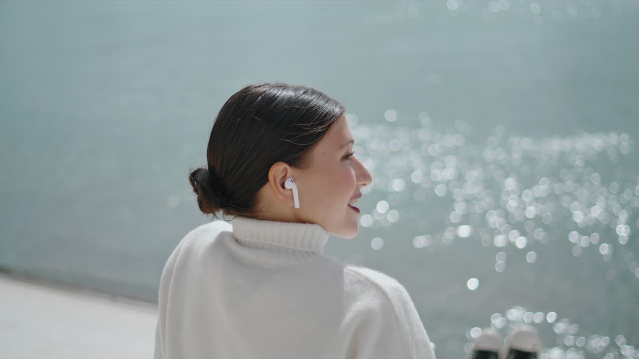 Young woman speaking wireless earphones sitting quay at weekend closeup vertical