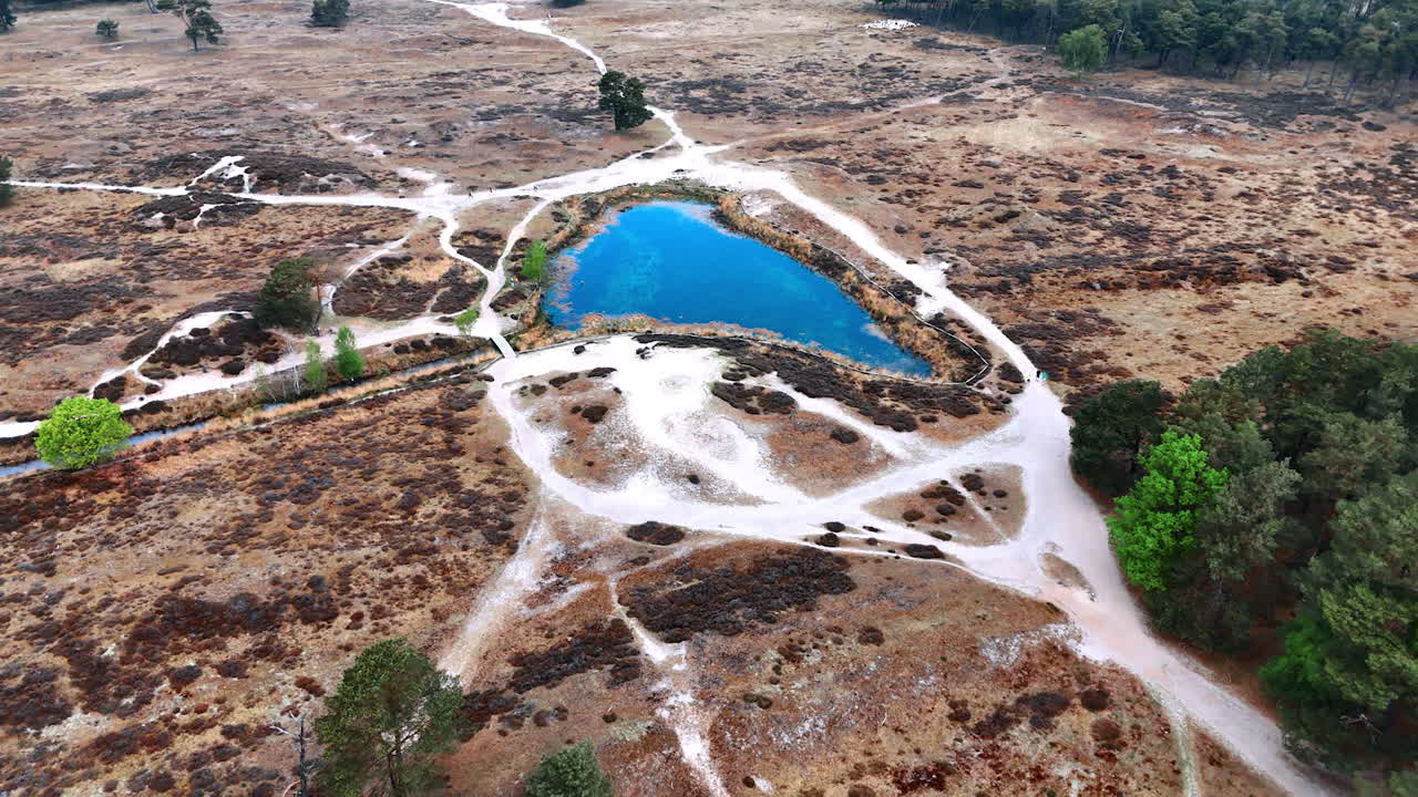 Calm blue lake in Dutch reserve. A calm blue lake nestled in the dry landscape and trails of a Dutch nature reserve by day