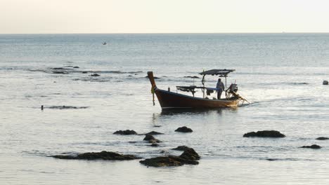 fisherman steering simple fish boat, hard labour on sea, koh lanta, thailand