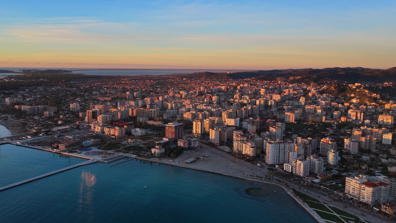 Aerial drone view of Vlora, Albania, showcasing the city's dense coastal skyline, mountain backdrop, and turquoise seafront