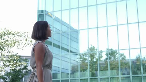 Elegante-Joven-Mujer-De-Negocios-Está-Mirando-Un-Rascacielos-De-Cristal-Y-Luego-Camina-Hacia-él-En-Un-Día-Soleado