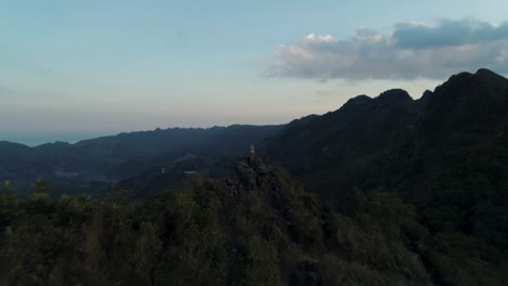 blond european travel girl with arms in air carefree on mountain peak at dusk