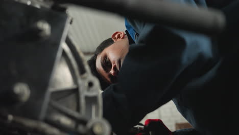 lower angle view of mechanic in blue uniform working on engine with red hand glove, focused on detailed repair and inspection in automotive workshop