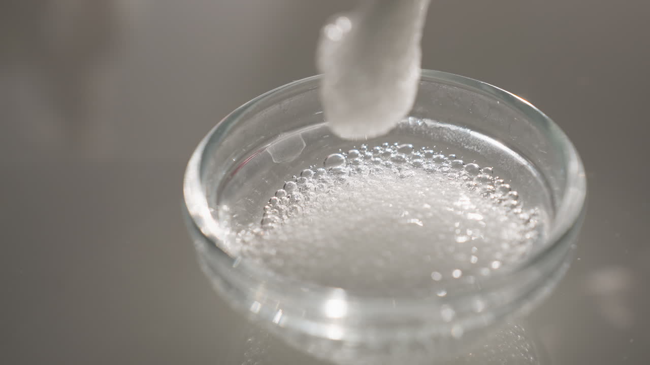 White gel bubbles gently lifted by silicone brush in glass bowl to test texture and consistency under soft light, highlighting skincare prep, sensory detail and professional facial treatment ritual