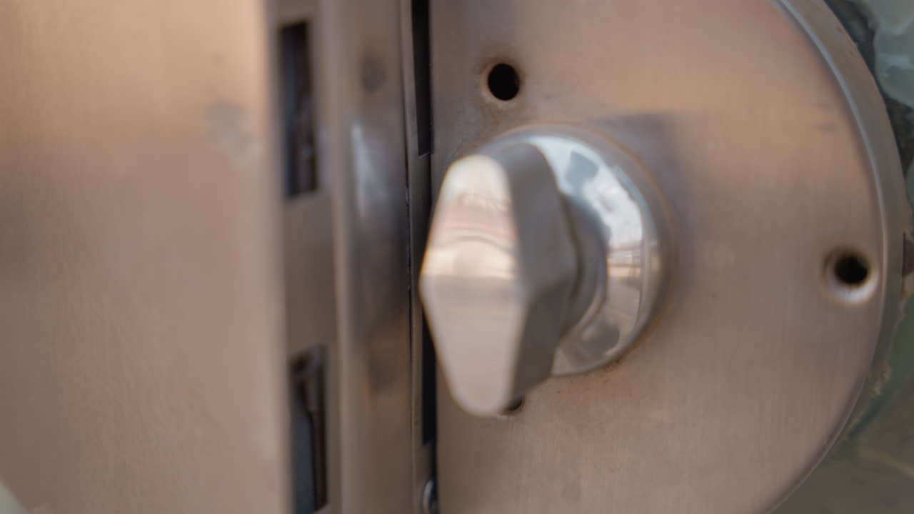 Primo piano di una serratura di sicurezza di una porta in serata, atmosfera di placido crepuscolo, controllo finale del proprietario di casa, pollice che ruota il chiavistello, soglia residenziale tranquilla, routine protettiva, sottili riflessi metallici, calde tonalità del tramonto.