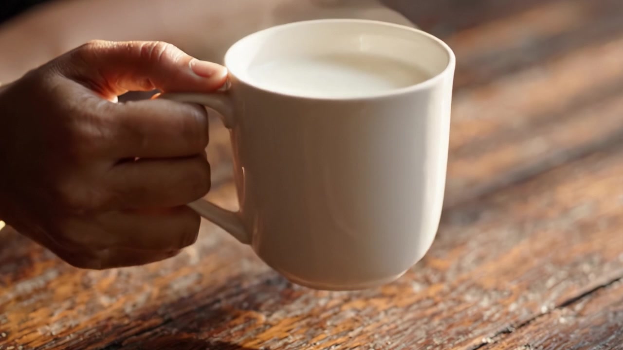 Una tazza di latte caldo fumante in mano, che evoca comfort e permette di assaporare momenti di tranquillità su un tavolo di legno rustico.