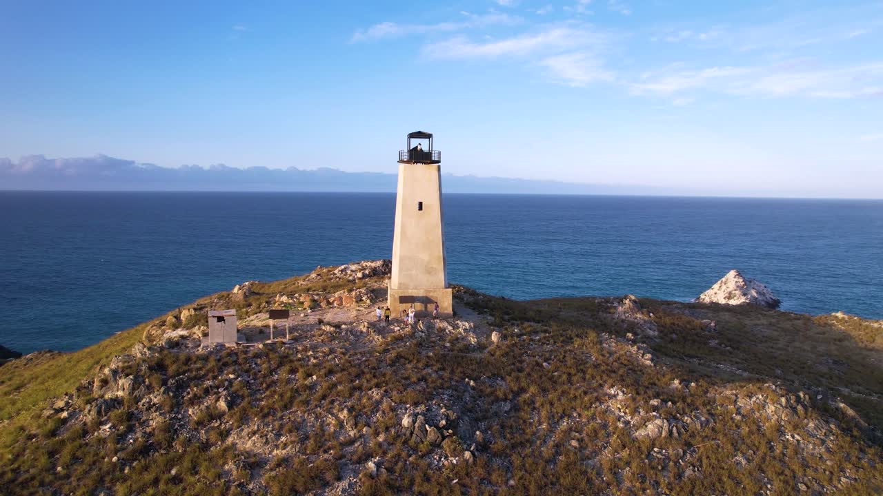 faro en ruinas con vistas al mar al atardecer con una ciudad costera en el fondo, vista aérea