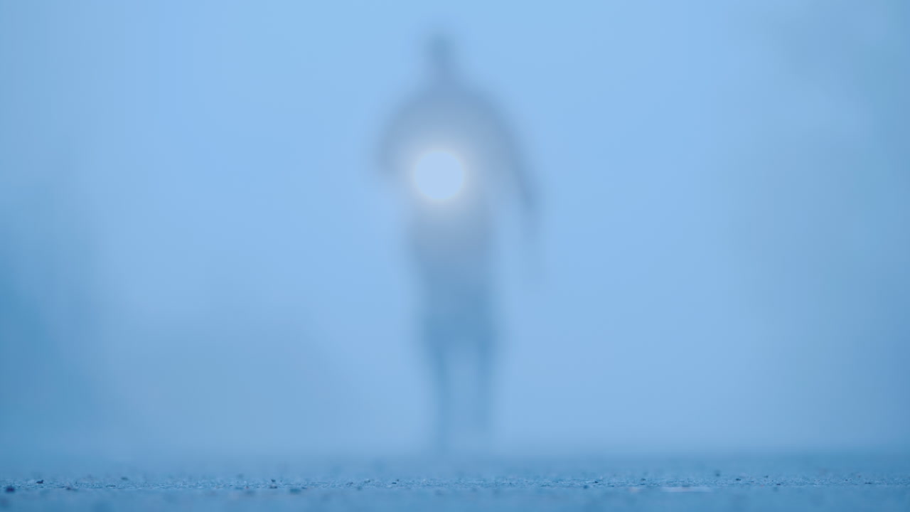 도끼와 손전등이 달린 피 묻은 도끼를 들고 안개 속에 있는 남자의 흐릿한 실루엣