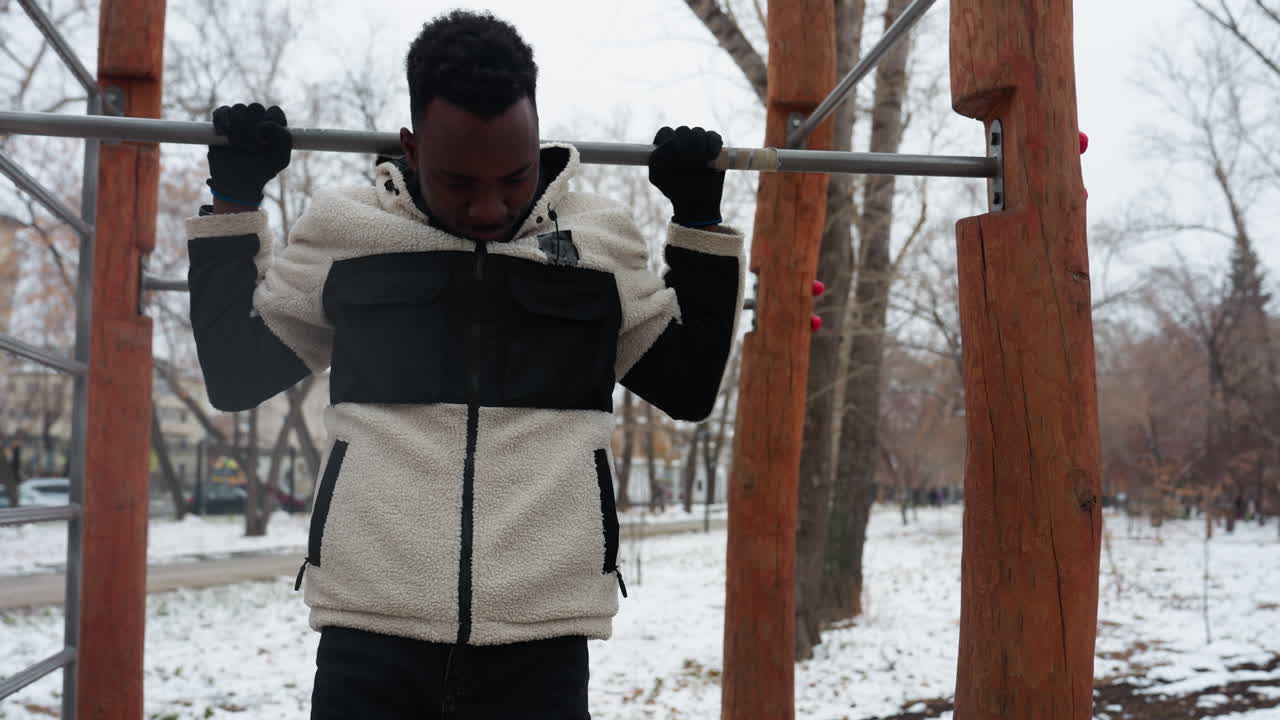 겨울 재을 입은 을 는 젊은이가 눈 인 공원에서 철로 된 바를 잡기 위해 뛰어내리고, 조용한 환경에서 벌거벗은 나무로 둘러싸인 노력 끝에 내려갑니다.