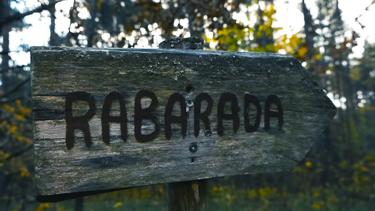 Close up view of a wooden sign that leads to marshland bog hiking trails during autumn morning with shallow depth of field and bokeh blurry yellow leaves in the background. Rabarada sign in Estonia