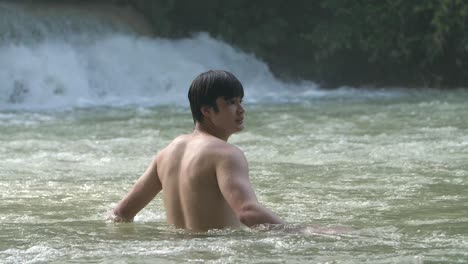 asian man relaxing in waterfall in tropical nature, slow motion