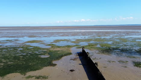 vuelo bajo de drones sobre un viejo espigón de madera y sobre marismas de un estuario de marea en una tarde brillante y soleada con un cielo azul brillante