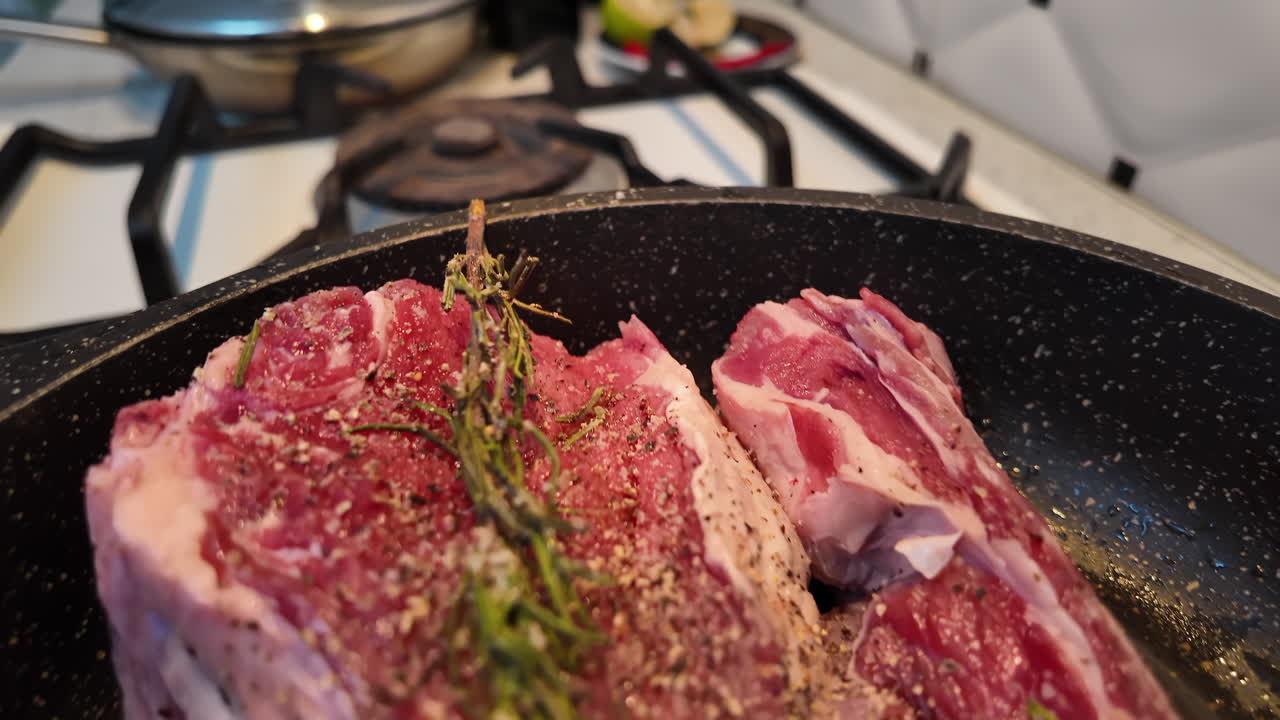 Big red beef stake on a black pan with rosemary ready for cooking, black pepper on top