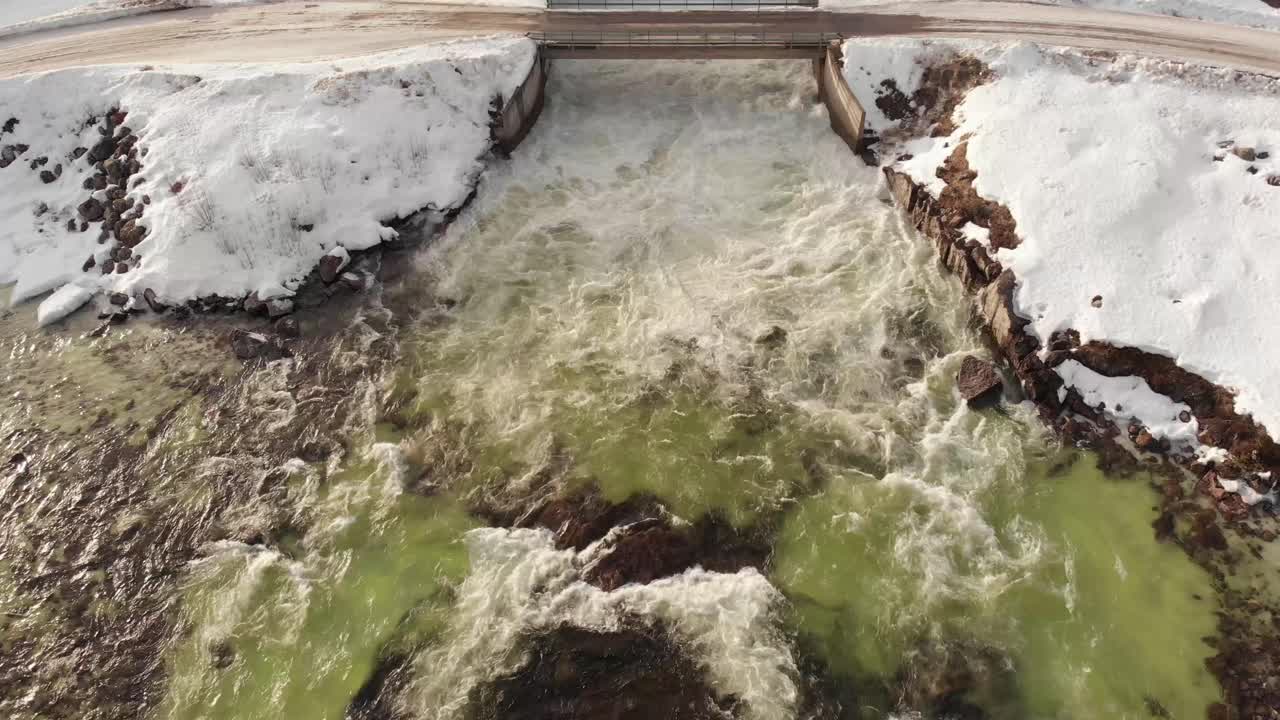Turbulent water from Dam's floodgate, streaming down icy cold cascade - static Bird's eye view aerial shot