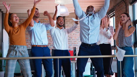 business team celebrating in multi-cultural office with colleagues throwing paperwork in the air