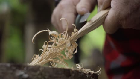 man shaving out wood with his knife to prepare for a handmade fire as part of the bush craft training workshop