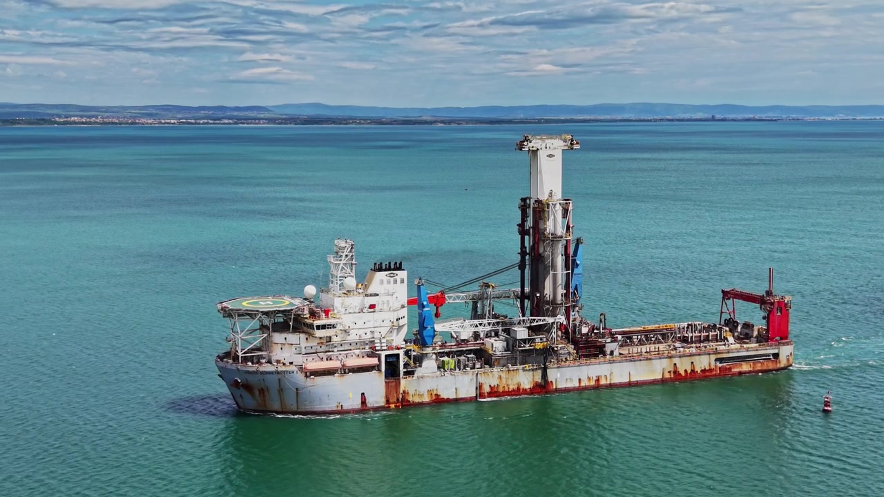 Large ship moves through calm waters near a coastal area in the daytime