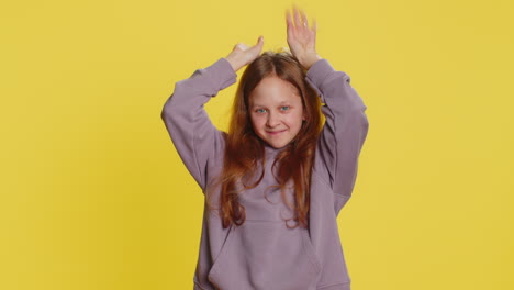 young girl makes bunny ears with her hands and smiles happily at the camera