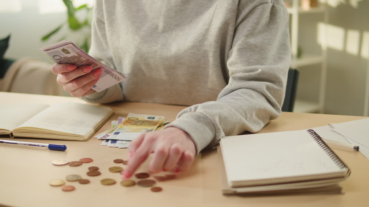 Donna che conta banconote e monete in euro mentre scrive su un taccuino
