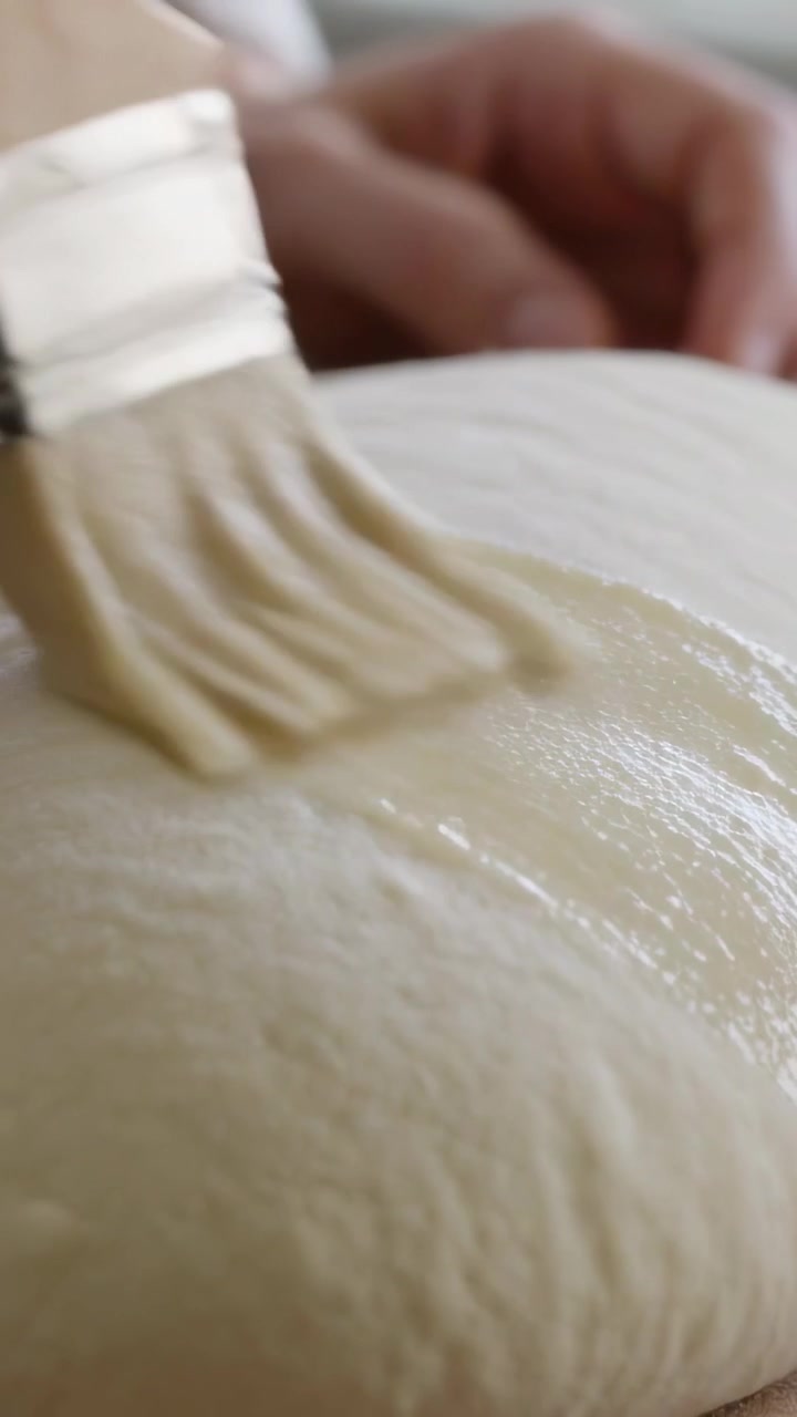 Vertical video: Brushing as brush enters bakers hands glazing risen dough to bake in kitchen sleeve