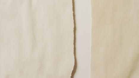 Video-of-close-up-of-torn-pieces-cream-paper-on-white-background