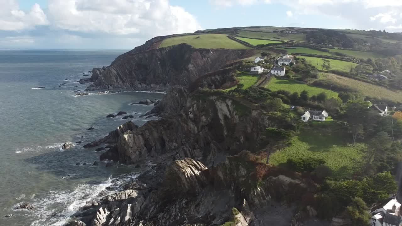 toma aérea en órbita de drones de un pueblo costero en la cima de un acantilado con olas rompiendo en formaciones rocosas debajo - lee bay, beach, ilfracombe, devon