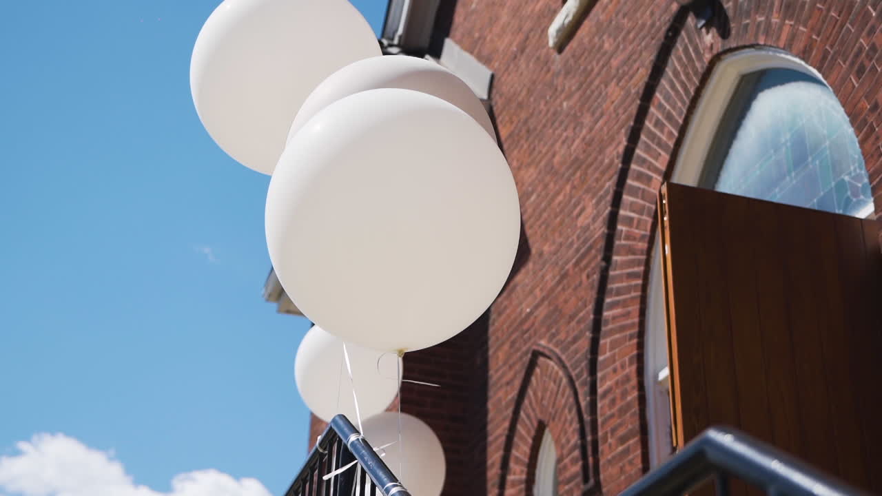 globos de boda blancos que soplan en la brisa fuera de una iglesia