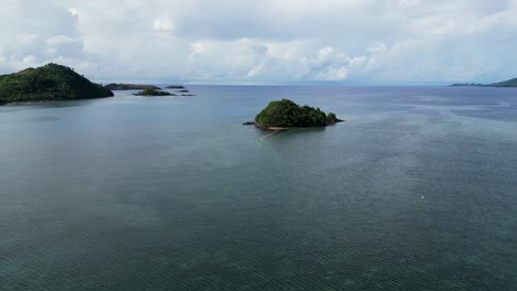 tiny island with trees in the ocean on a cloudy day, aerial dolly forward