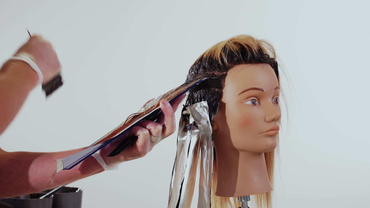 Plano medio de una cabeza de entrenamiento de peluquería donde el peluquero aplica tinte con un pincel