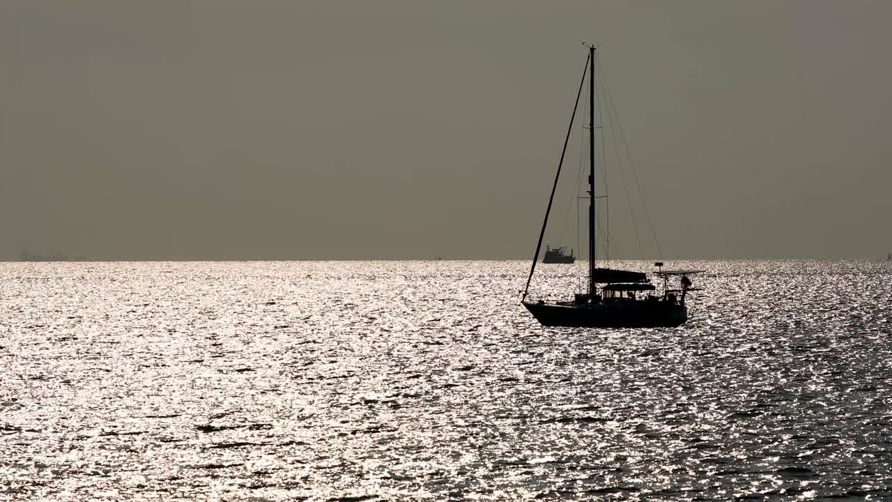 Silhouette of a Yacht on the Ocean Horizon with Sunlight Reflecting of the Calm Waters in Bangsaray near Pattaya, Thailand. Zoom Shot in 4K