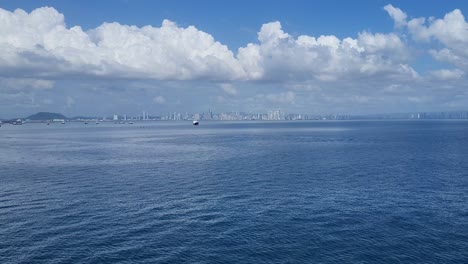 distant aerial view of panama city skyline across calm ocean water under a blue sky with clouds.
