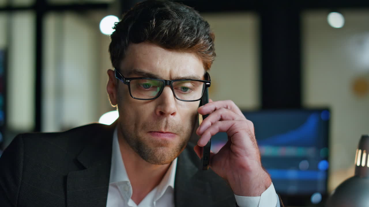 Primo piano di un manager stressato che parla al cellulare in ufficio, con statistiche sugli investimenti.
