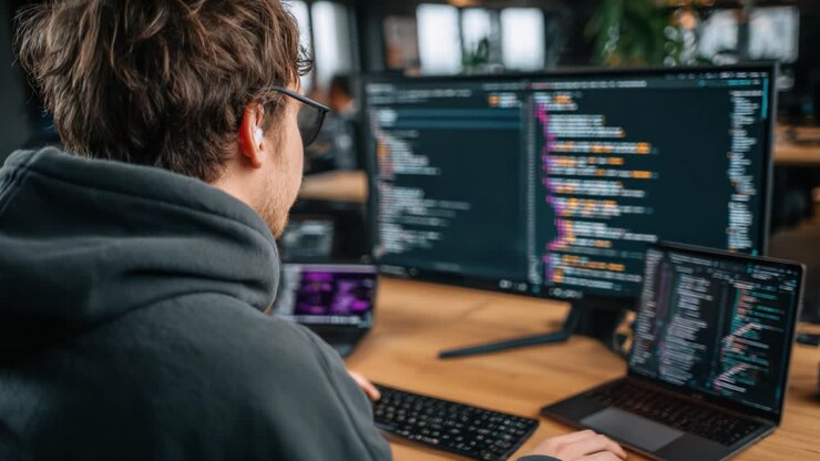 An engaged programmer working intently at a modern workspace, focused on dual screens displaying complex code amidst a vibrant tech environment, highlighting digital creativity