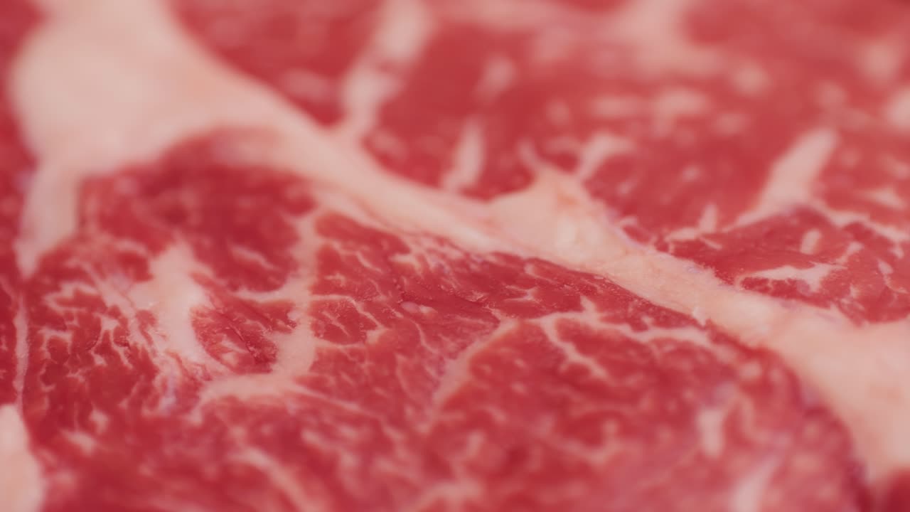 胡椒、塩、ローズマリーが添えられた新鮮な霜降り牛肉のクローズアップマクロ映像。グリルでジューシーなステーキを調理する準備。プレミアムなオーガニック生和牛肉。高品質4K映像。