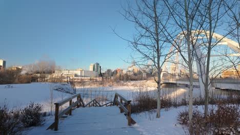 walking towards the left side of walterdale bridge, showcasing highrise buildings downtown edmonton. a snowy river valley, and the cold beauty of the city