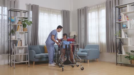 cuerpo lleno de enfermero masculino asiático ayudando al paciente en silla de ruedas usando un andador para estar de pie por sí mismo durante una terapia física en casa