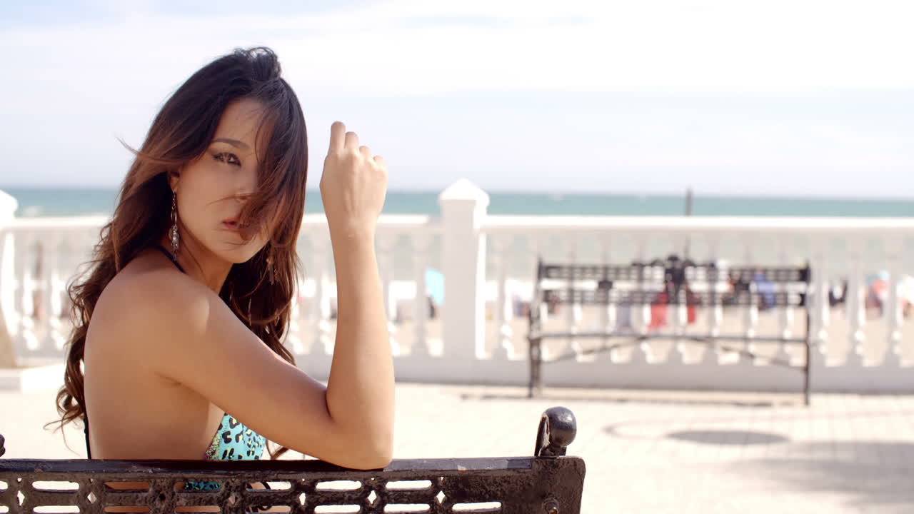 젊은 여성이 바다의 벤치에서 휴식을 취하고 있습니다.