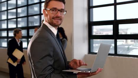 hombre de negocios de pie usando una computadora portátil y sonriendo a la cámara