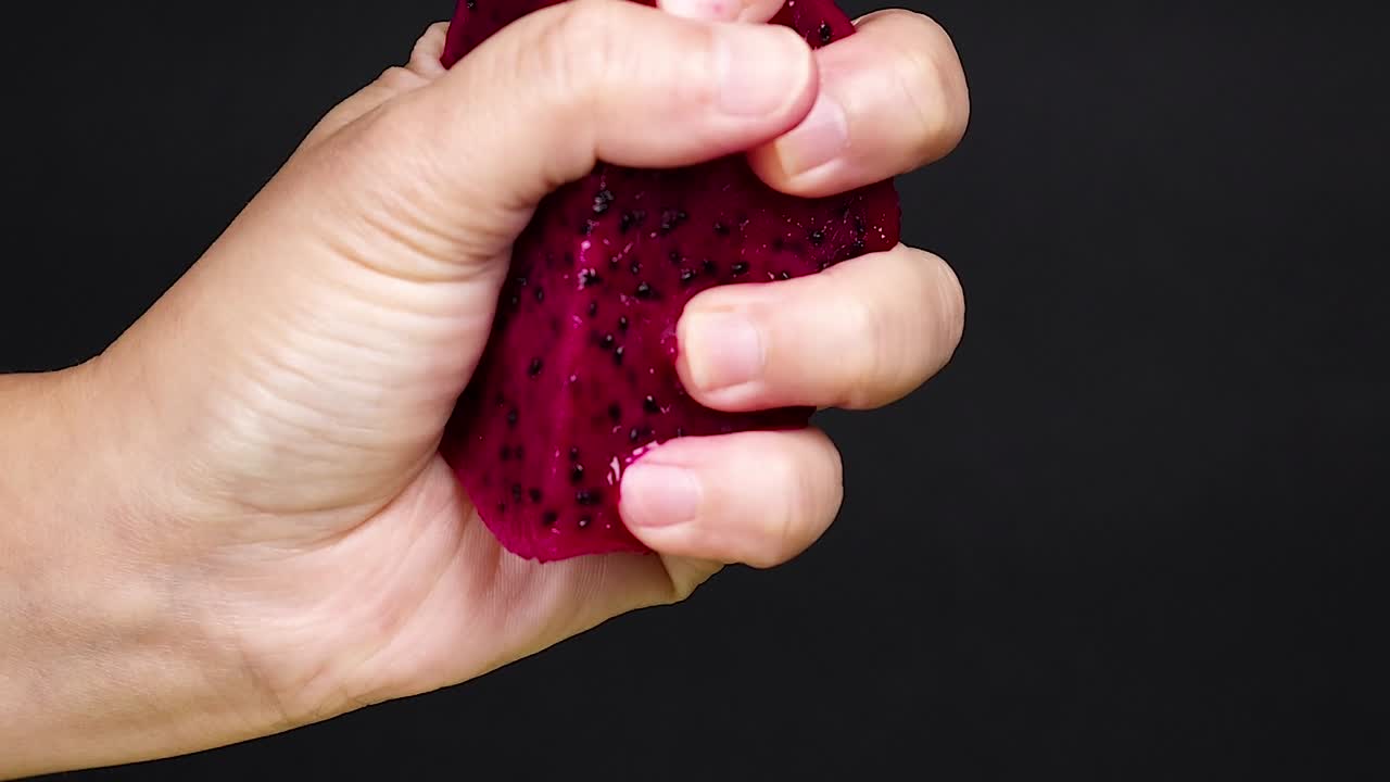 A hand tightly squeezes vibrant red pulp, releasing juice and seeds in a dynamic motion.