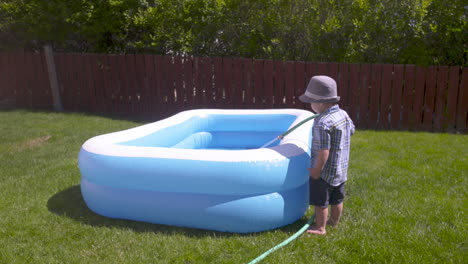 Little-boy-filling-his-backyard-pool-with-a-hose-on-a-hot-summer-day