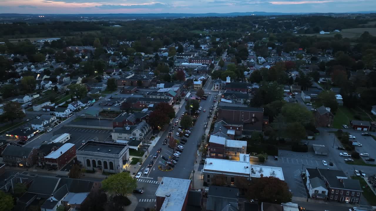 vista aérea de una pequeña ciudad al anochecer con coches en la calle principal y las casas circundantes