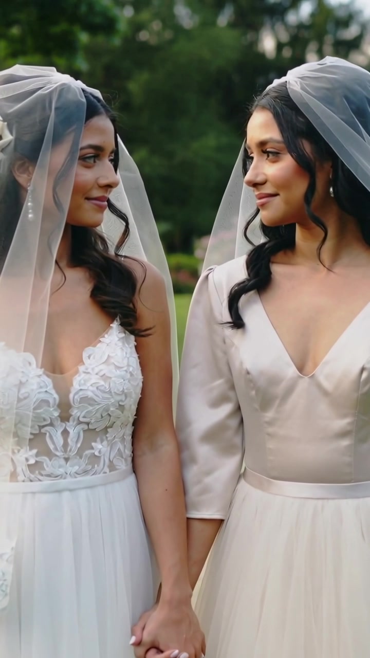 Vidéo verticale : Zoom de la caméra sur des mariées en robe se tenant la main, se tournant l'une vers l'autre dans un jardin pour échanger leurs vœux.