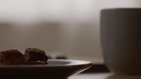 close up of plate of chocolate brownies next to person drinking hot drink from mug 1