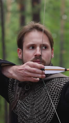 concentrated bearded archer shoots bow in green wood closeup slow motion. medieval warrior attack aim at battle. historical weapon at war action