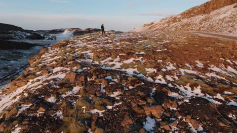 un hombre parado al borde de una montaña erosionada y operando el dron para capturar la hermosa puesta de sol sobre la tierra volcánica en islandia