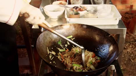 kuy teav cha or cambodian stir-fried egg noodle being cooked in a traditional wok at a streetfood stall shot in slow motion