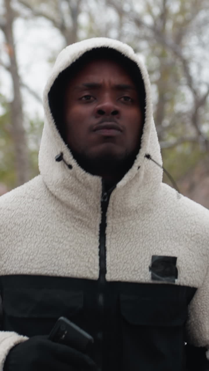 молодой взрослый в белой капюшоне бегает на открытом воздухе с размытым фоном деревьев и зданий, демонстрируя активный образ жизни и физическую подготовку в естественной обстановке в дневное время