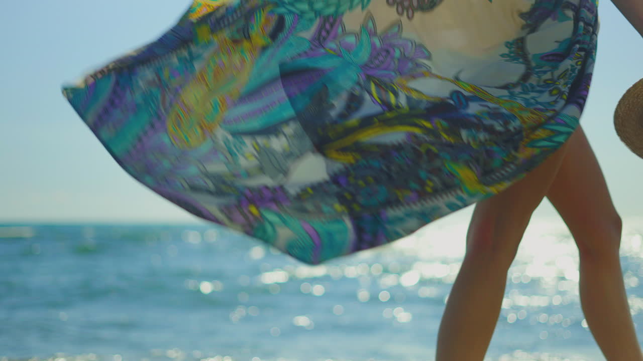 mujer caminando por la playa con un vestido impreso y un sombrero de paja