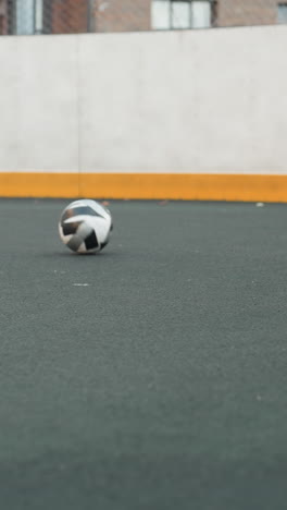 vista de la pierna de un individuo driblando hábilmente una pelota de fútbol en la superficie de la arena deportiva durante la sesión de entrenamiento, demostrando precisión y agilidad, el fondo incluye cercas de enlace de cadena y meta borrosa